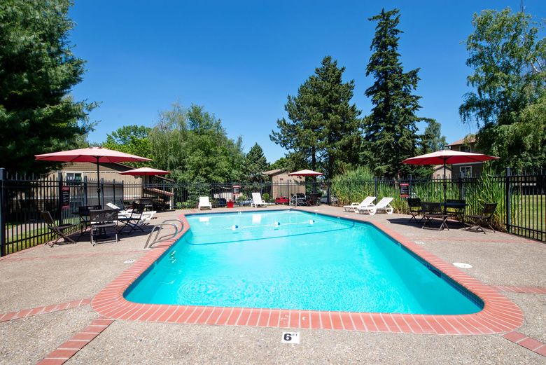 Outdoor swimming pool with lounge chairs, red umbrellas, and trees on a sunny day