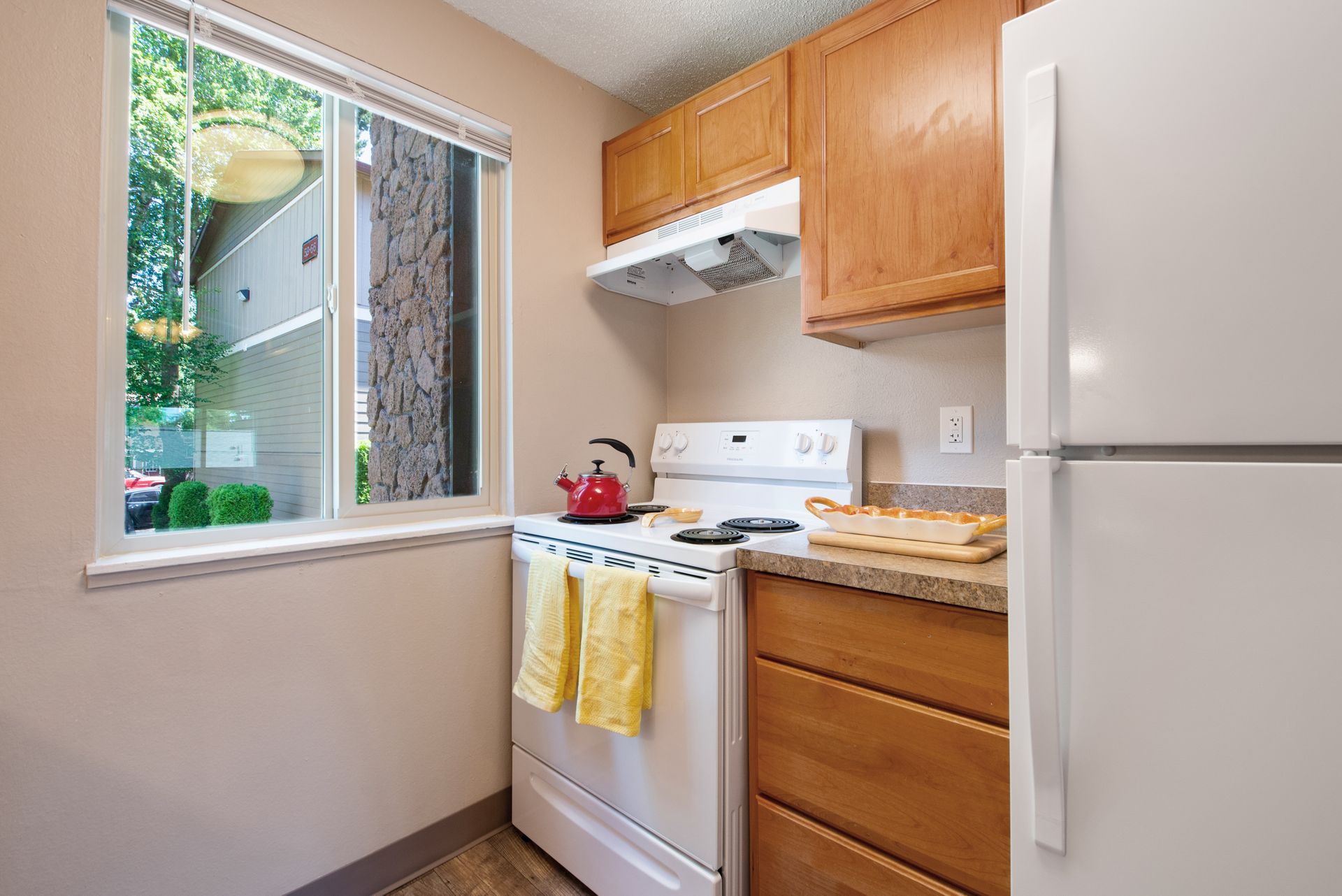 Small kitchen with white appliances, wood cabinets, and a window above the sink.
