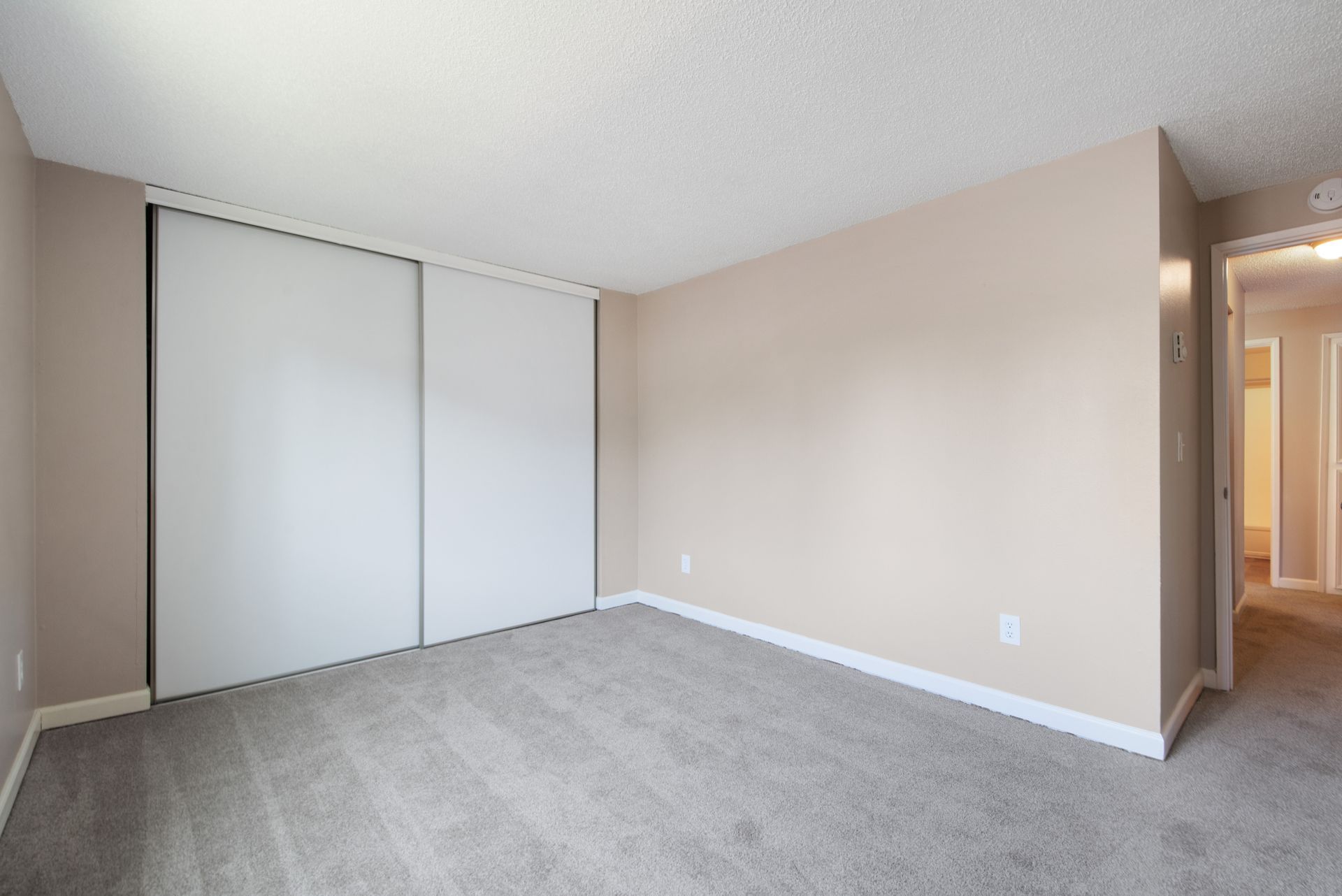 Empty beige bedroom with gray carpet and sliding closet doors