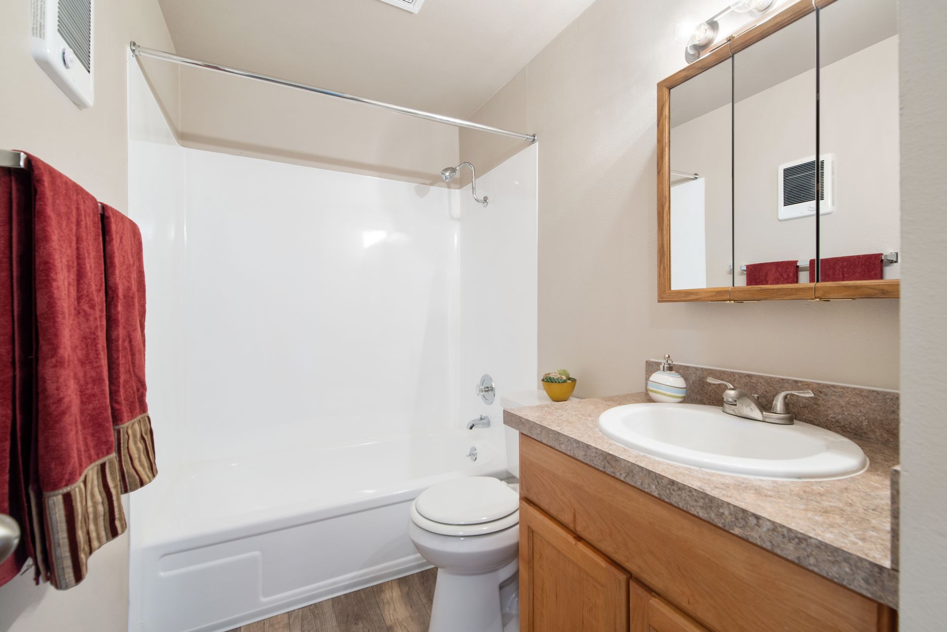 Small bathroom with shower-tub, toilet, and wood vanity with sink and mirror.