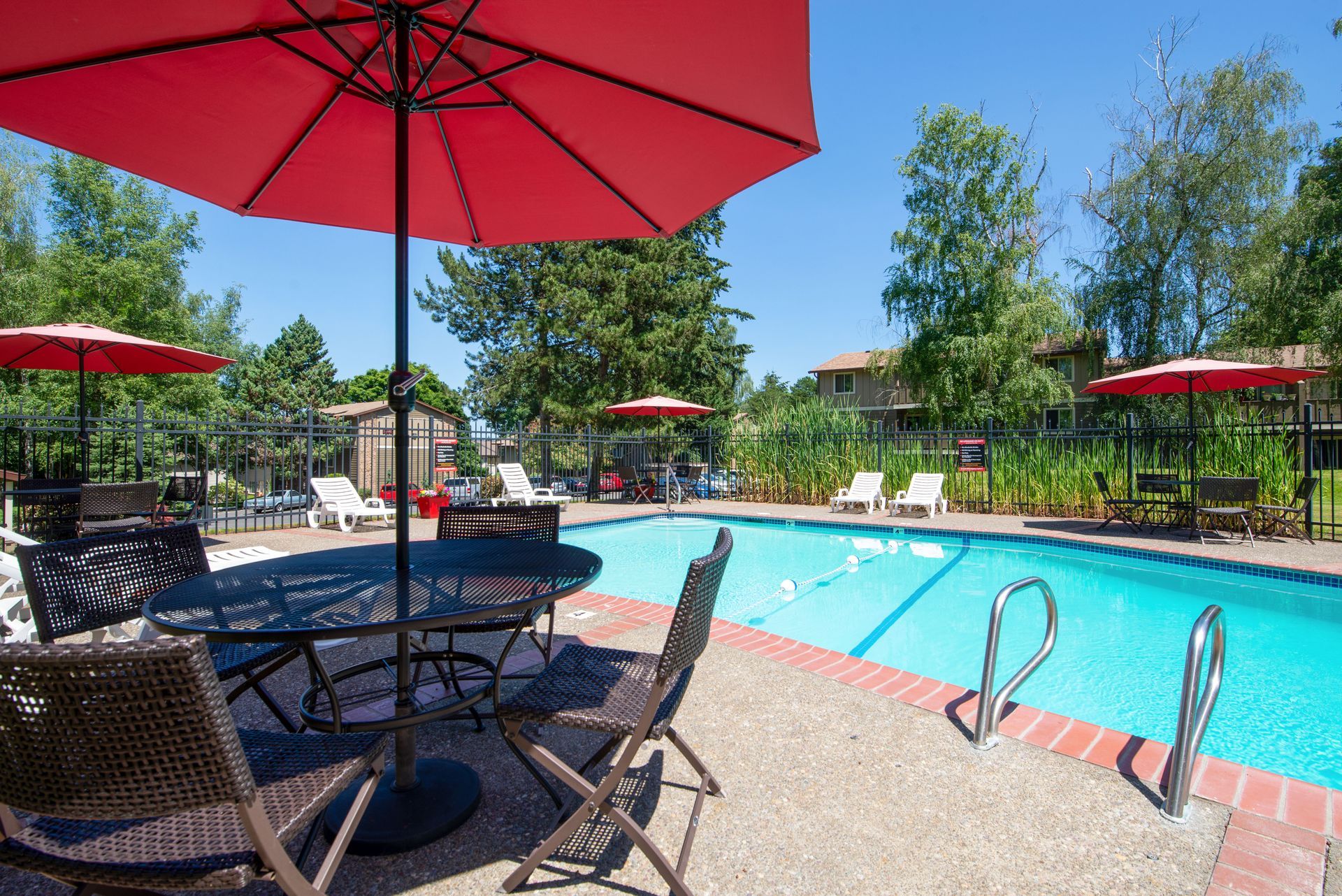Outdoor swimming pool with red umbrellas, lounge chairs, and trees on a sunny day