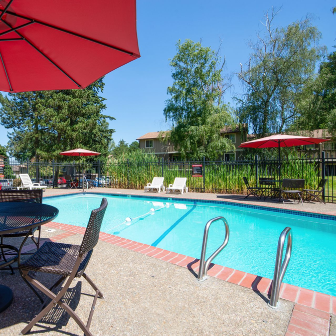 Outdoor swimming pool with red umbrellas, lounge chairs, and a metal ladder on a sunny day