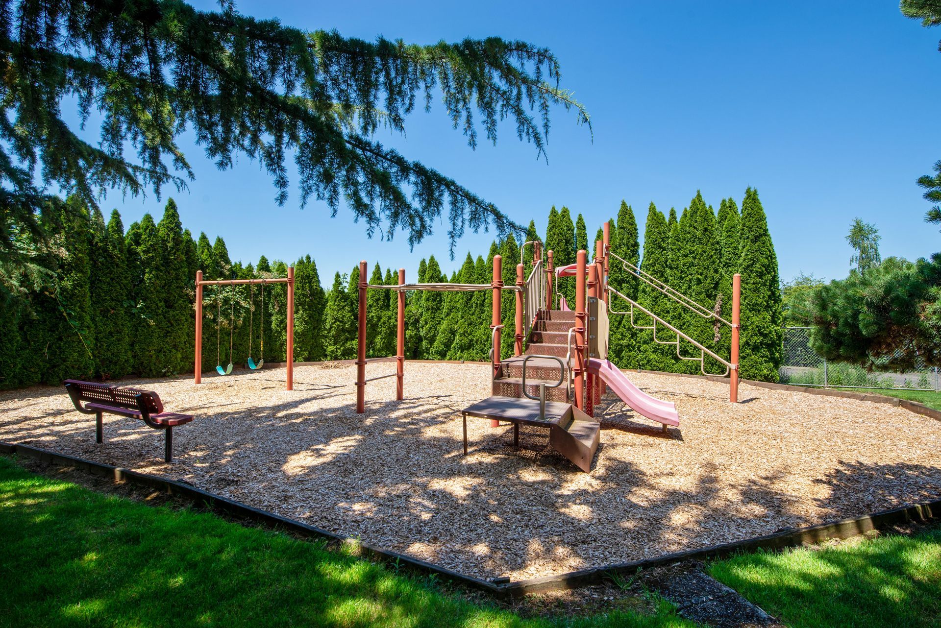 Outdoor playground with wooden climbing structures, slide, and gravel surface under a bright blue sky