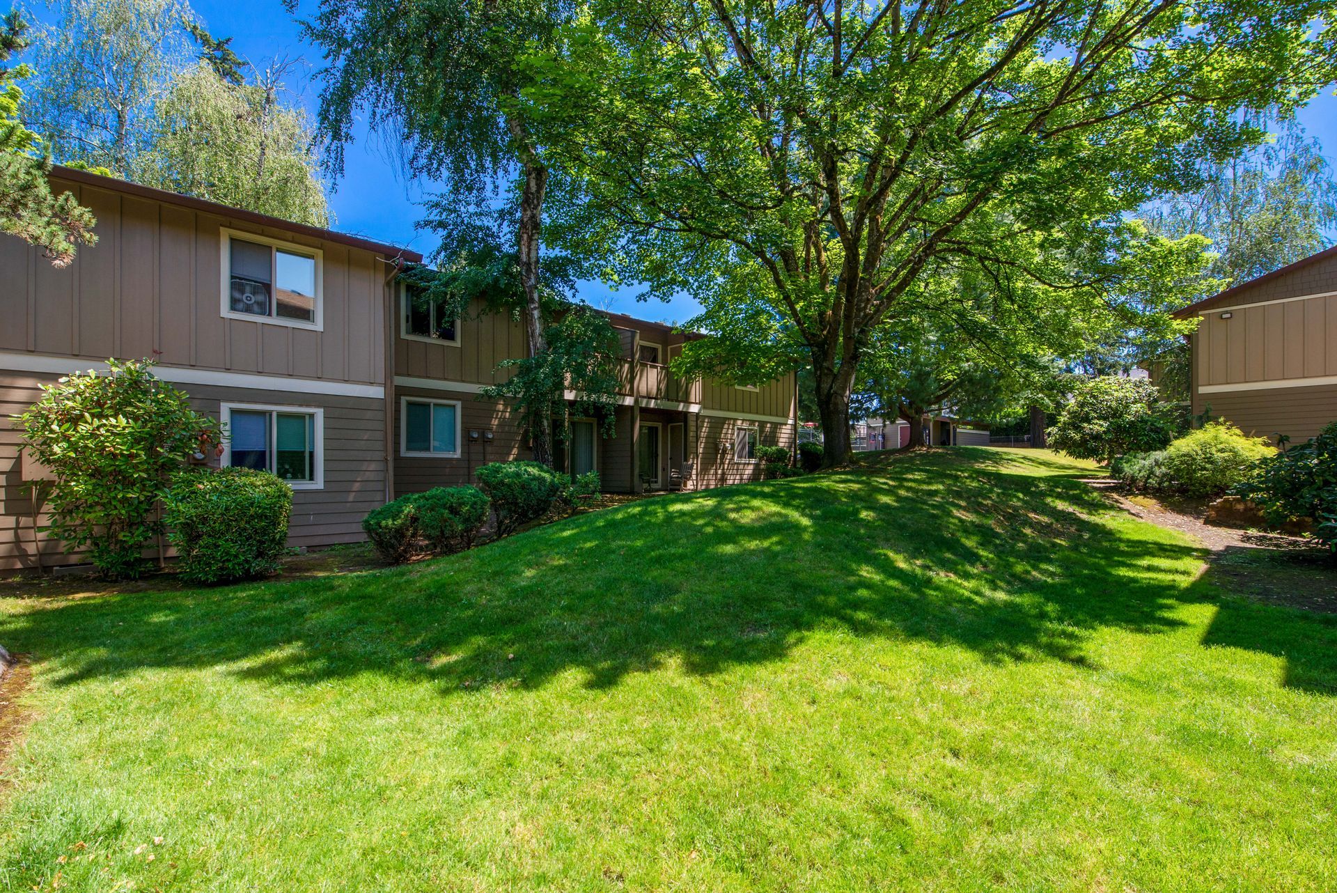Apartment courtyard with green lawn, trees, and brick buildings under a bright blue sky