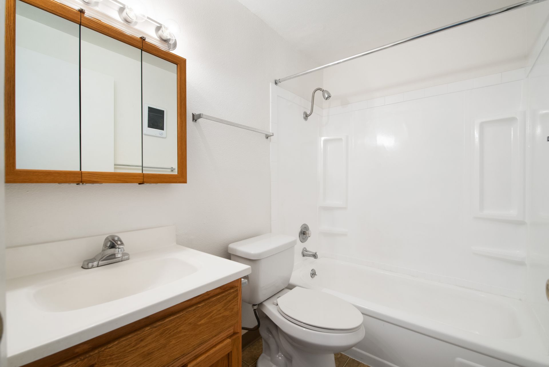 Small white bathroom with vanity, mirror cabinet, toilet, and bathtub shower.