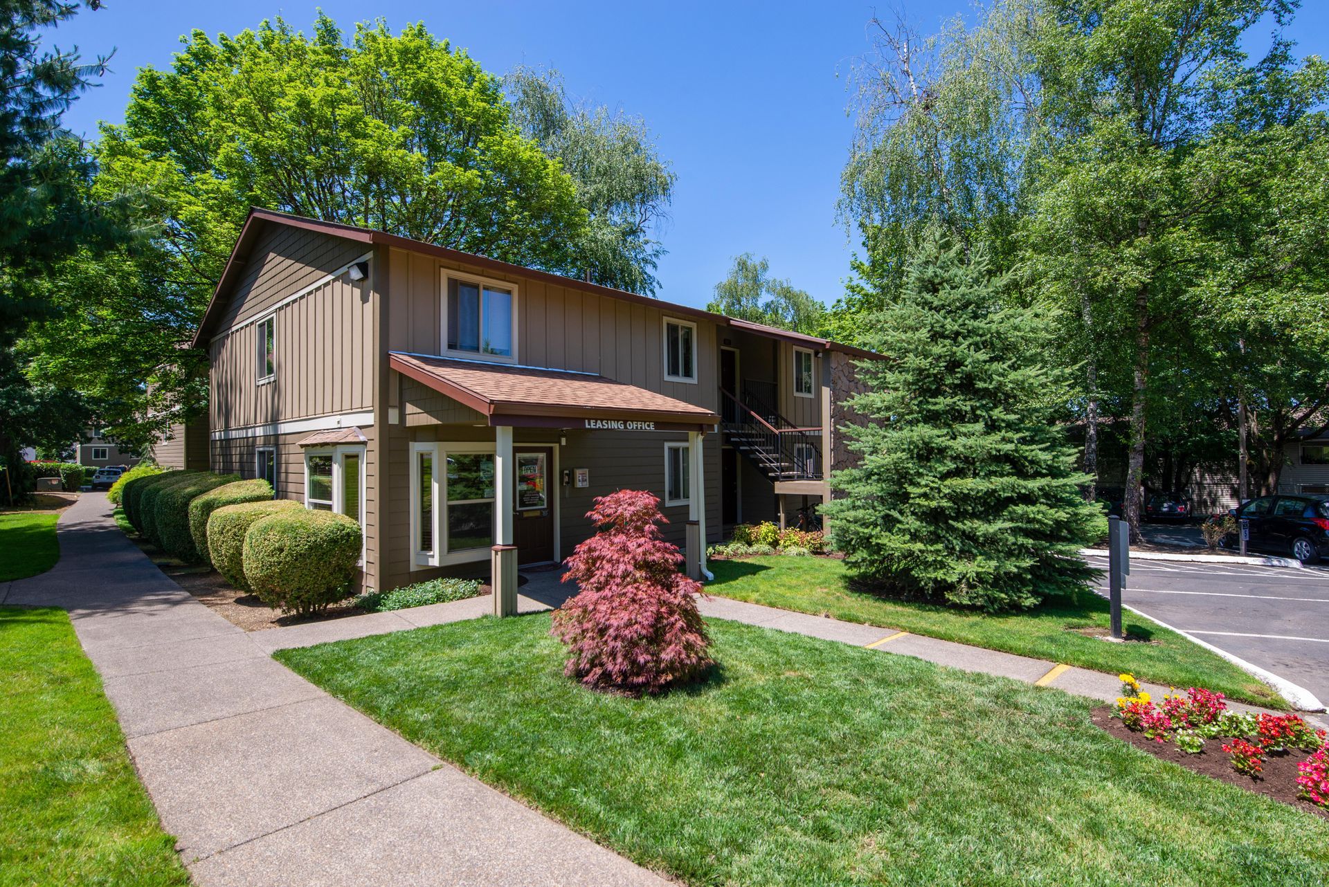 Two-story townhouse with manicured lawn, walkway, and trees under a bright blue sky