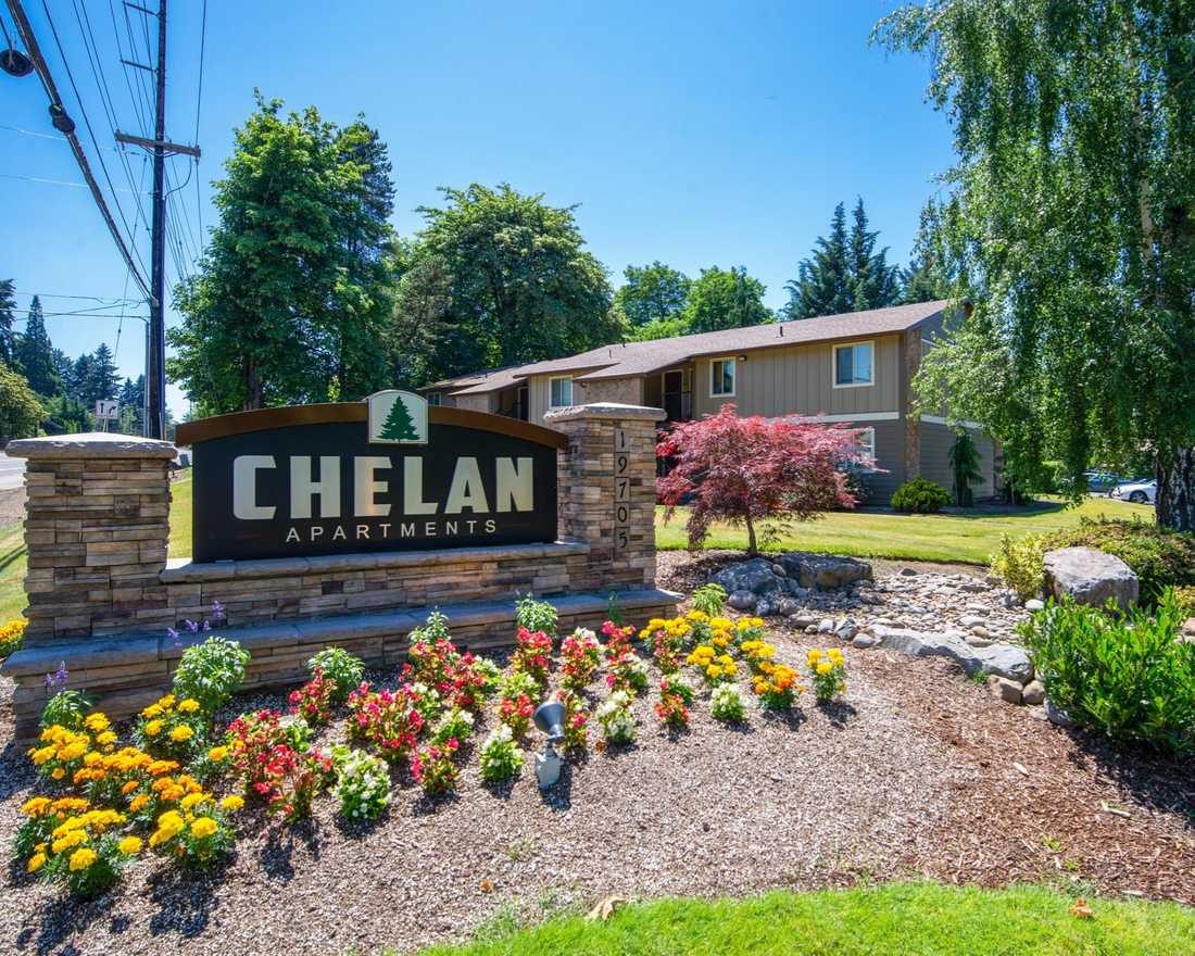 Chelan Apartments sign with colorful flower beds and a tan apartment building in the background