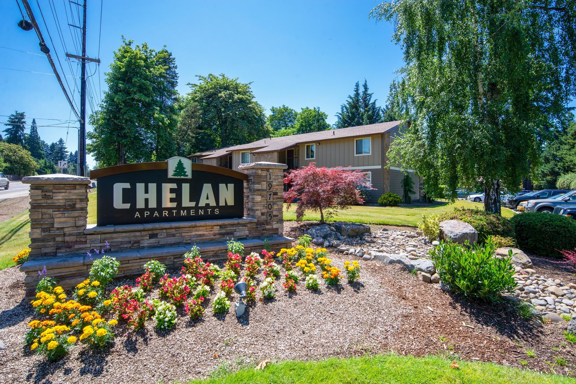 Chelan city sign in a landscaped flower bed with a brick building and trees behind it