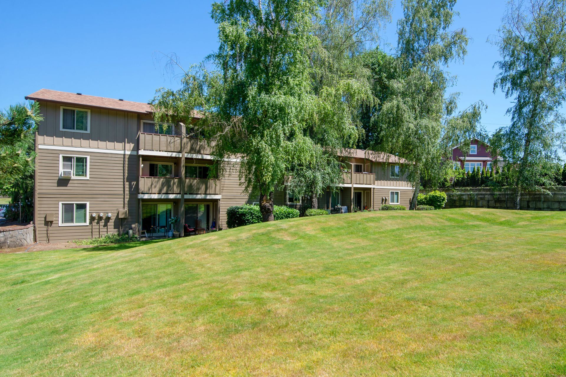 Apartment building beside a large green lawn with trees under a bright blue sky