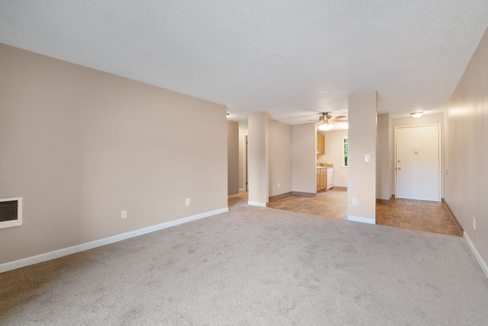 Empty beige living room with carpet, white columns, and hardwood entry area