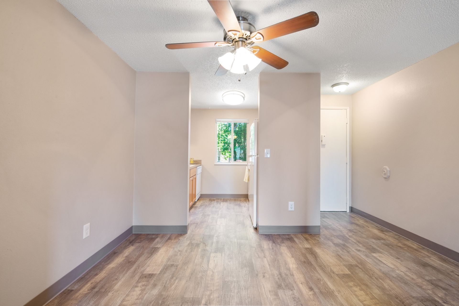 Empty living room with wood flooring, ceiling fan, and a window view into the next room.