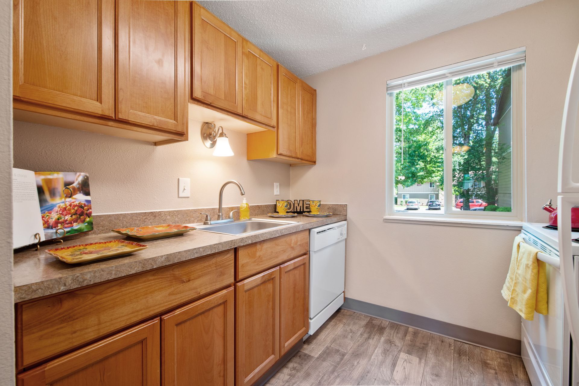 Small kitchen with wood cabinets, granite counter, white appliances, and a window overlooking greenery.