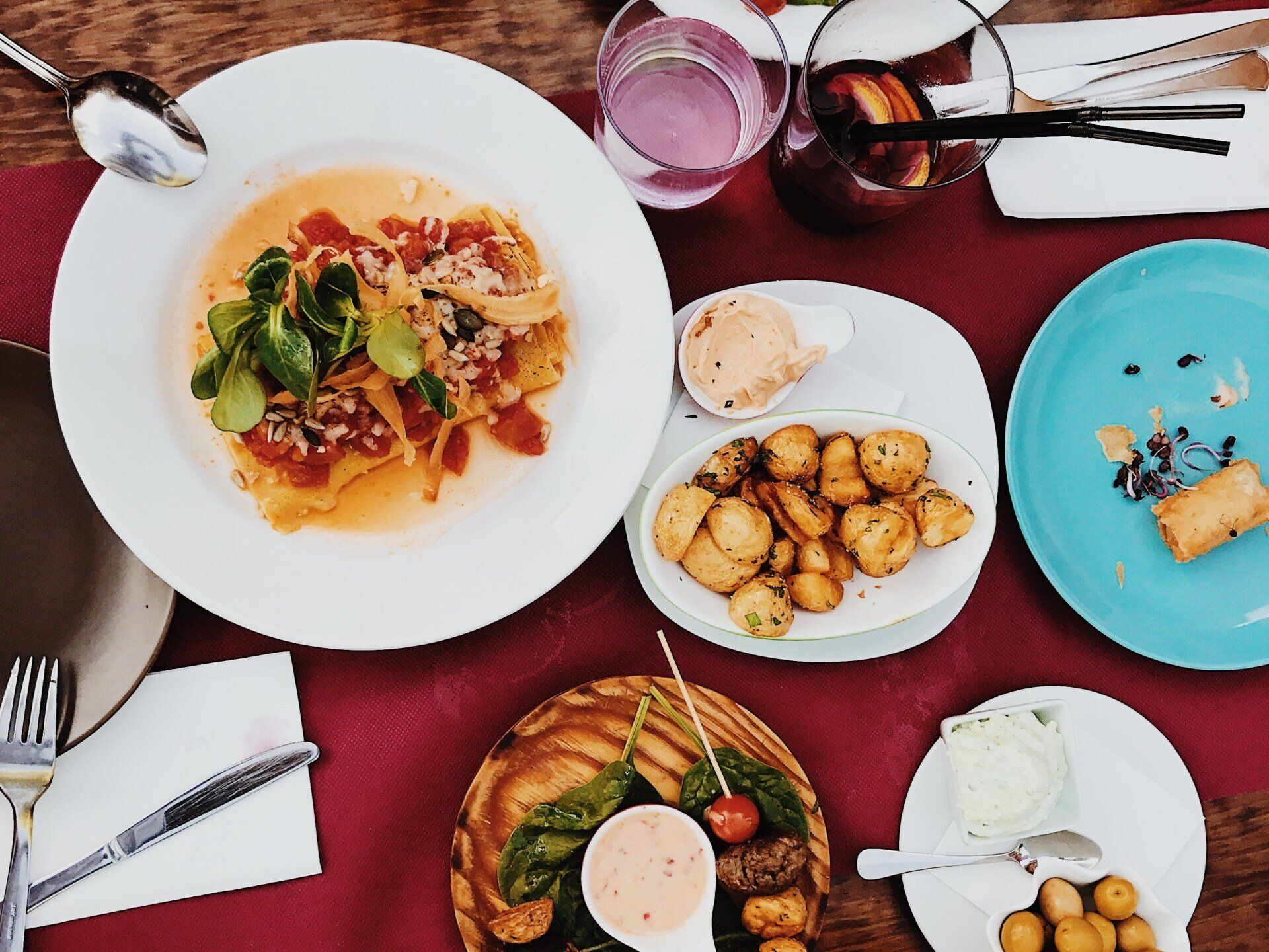 Overhead view of a table with colorful plated dishes, bowls, drinks, and utensils on a red tablecloth