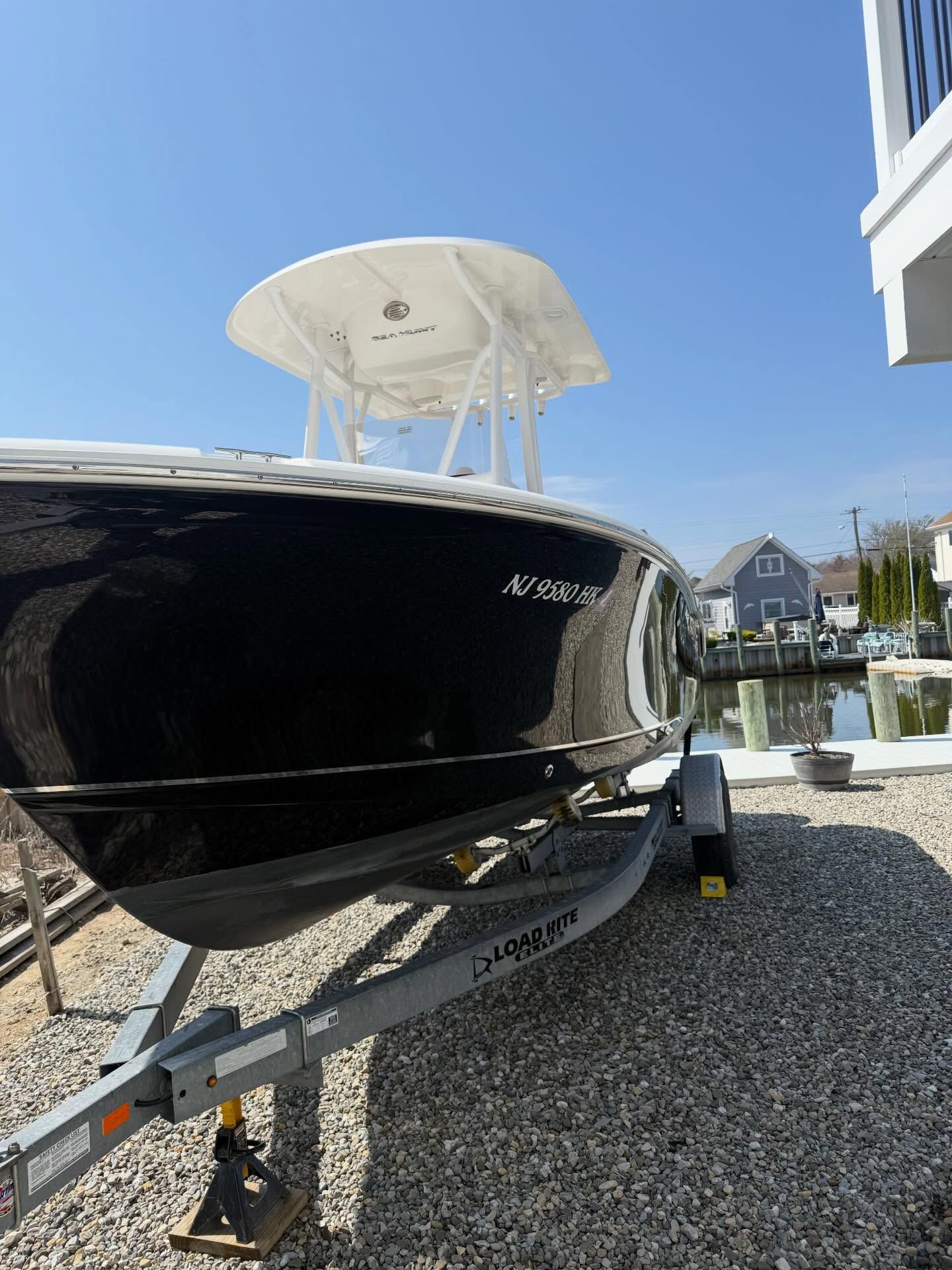 Black motorboat on a trailer beside a waterfront, with a white canopy and sunny blue sky