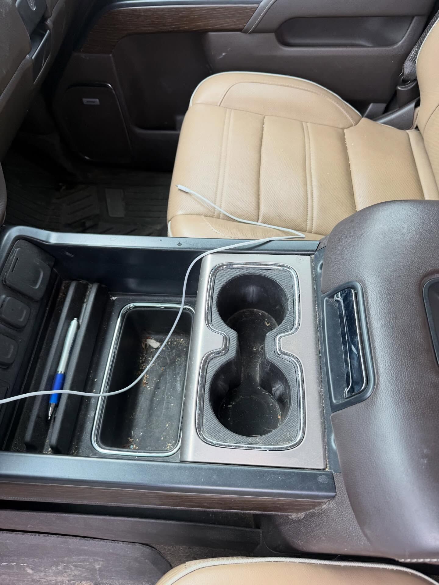 Car interior with tan passenger seat and center console cup holders, storage tray, and charging cable.