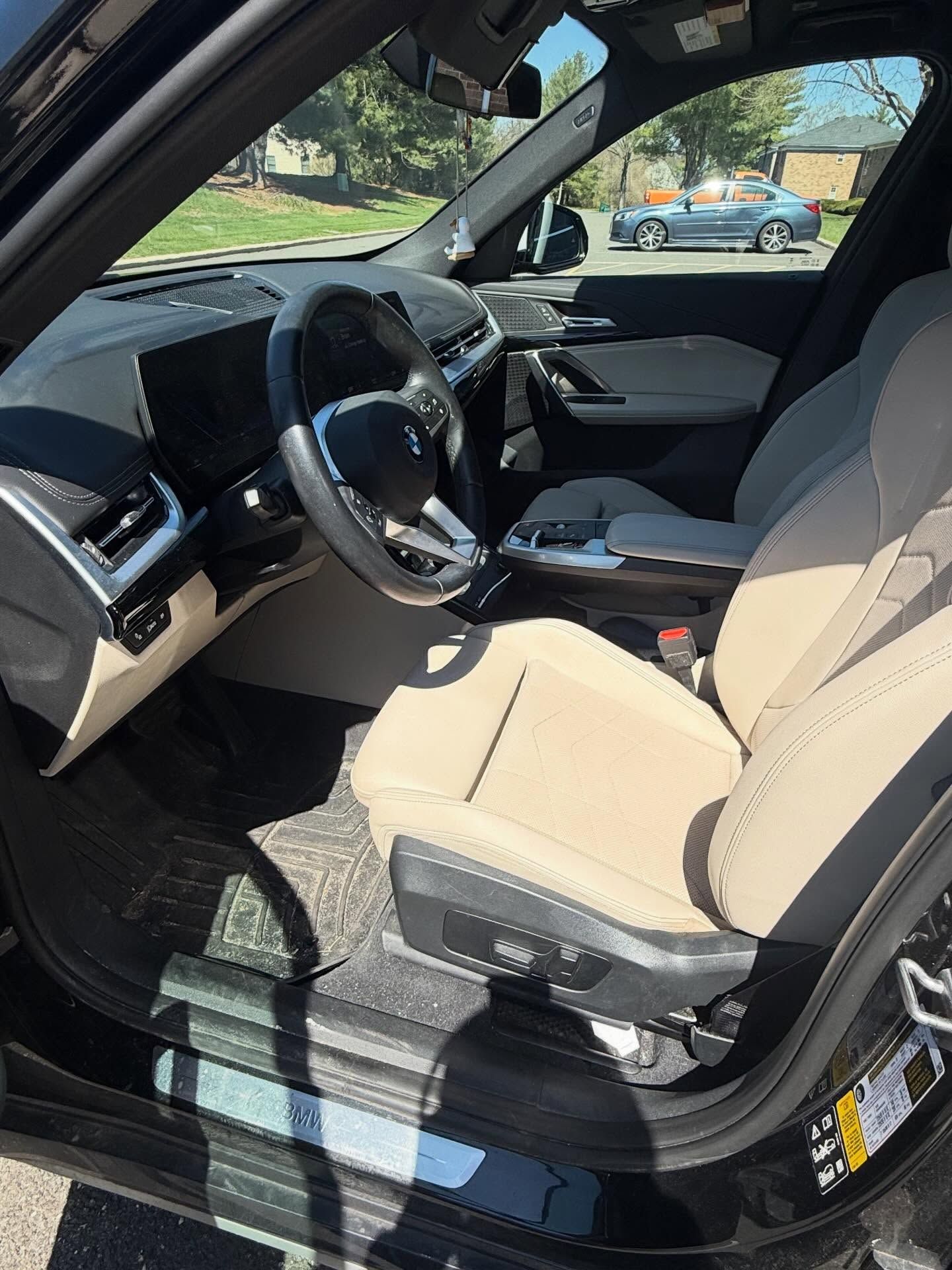 Car interior with beige seats and steering wheel, viewed from the open driver’s door.