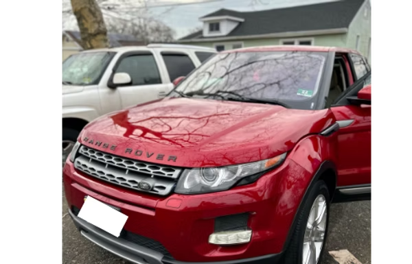 Red SUV parked beside a white vehicle near a house, with a tree reflected on the hood.