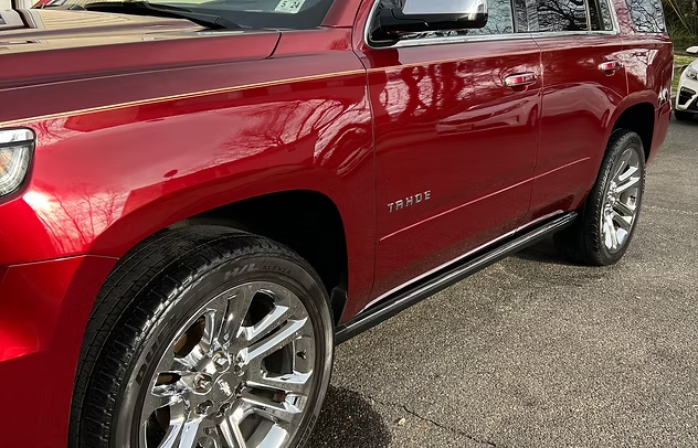 Red Chevrolet Tahoe SUV parked on pavement, showing the front side and chrome wheel.