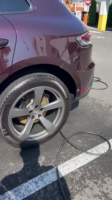 Maroon SUV charging at a public EV station, rear wheel and cable visible on pavement.