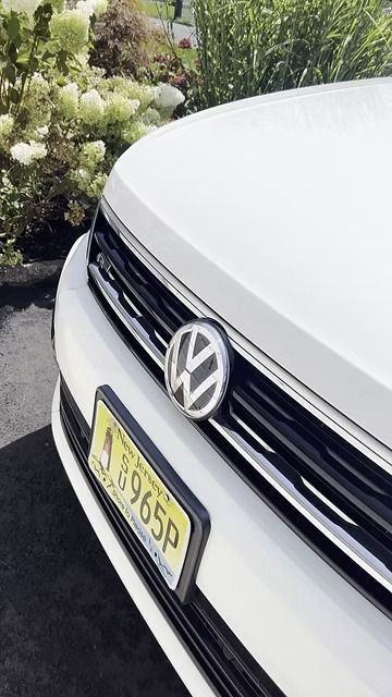 Front of a white Volkswagen with a yellow license plate parked beside greenery