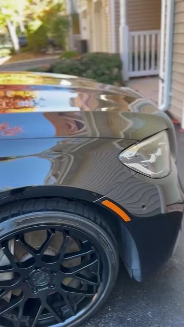 Dark gray sports car front fender and wheel parked in a driveway near a house.