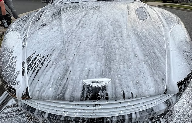 Foam-covered car front covered in thick white soap suds during a wash