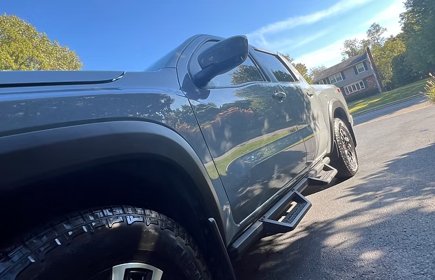Gray pickup truck parked on a driveway in bright sunlight, angled low from the side