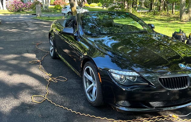 Black BMW convertible parked on a tree-lined driveway with a chain on the ground