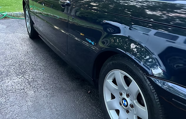 Dark blue BMW side view parked on wet pavement, front wheel visible