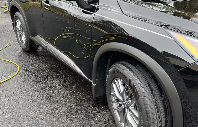 Black SUV with yellow cable draped over the side, parked on wet pavement near a silver car.