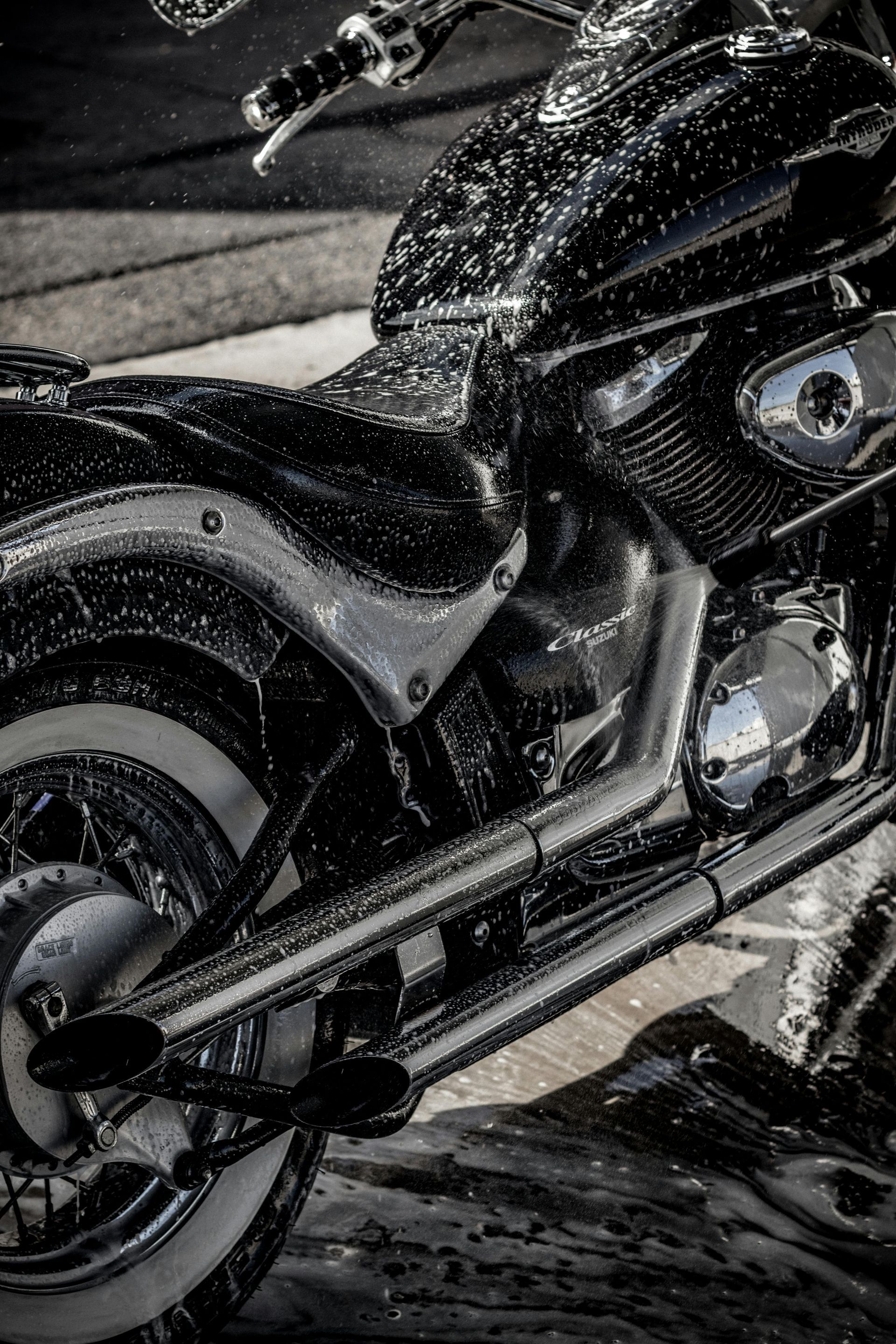 Black motorcycle with chrome exhaust and rear wheel, parked on a wet street at night