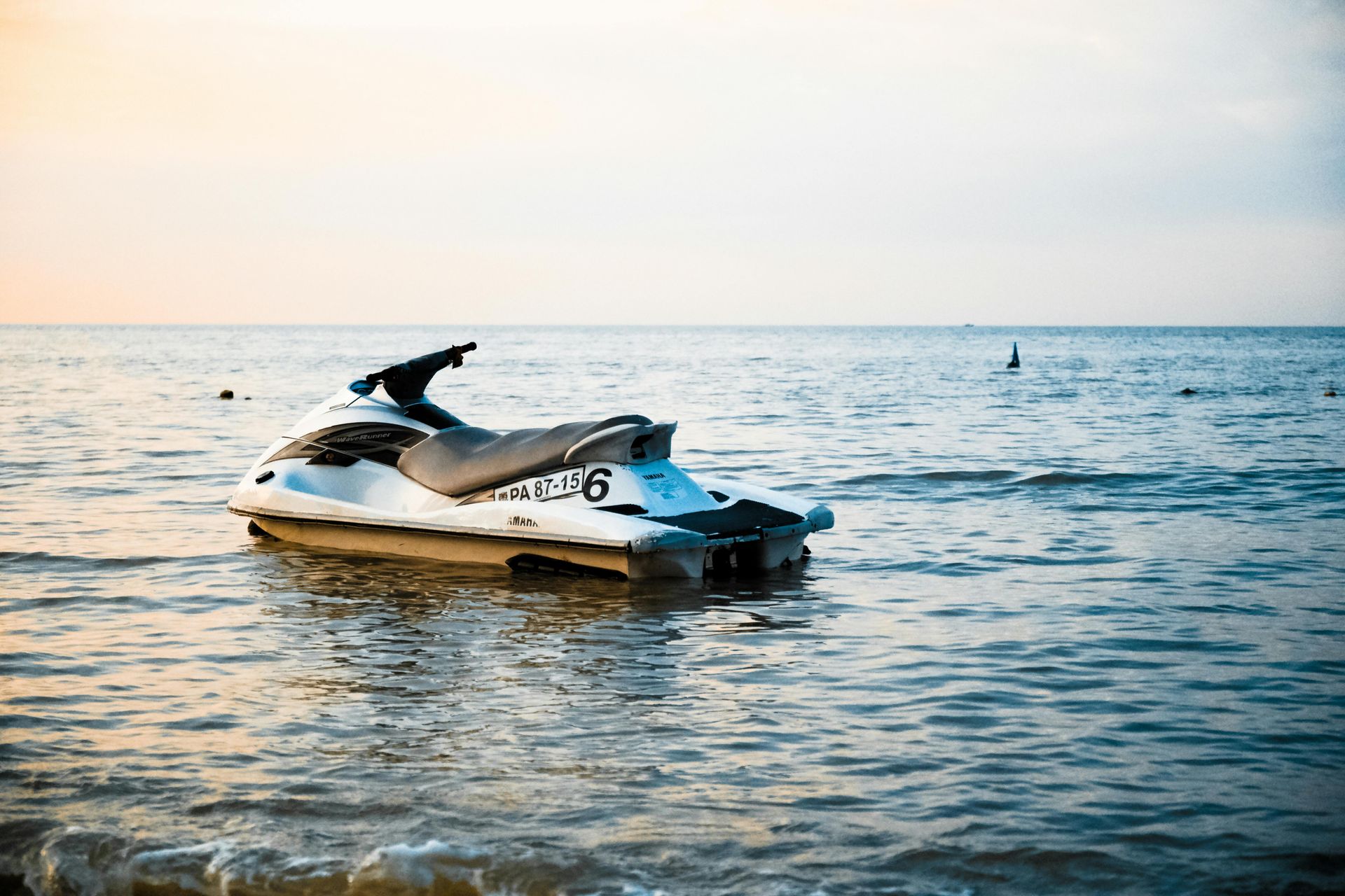 Jet ski floating on calm water at sunset, with a distant shoreline and orange sky