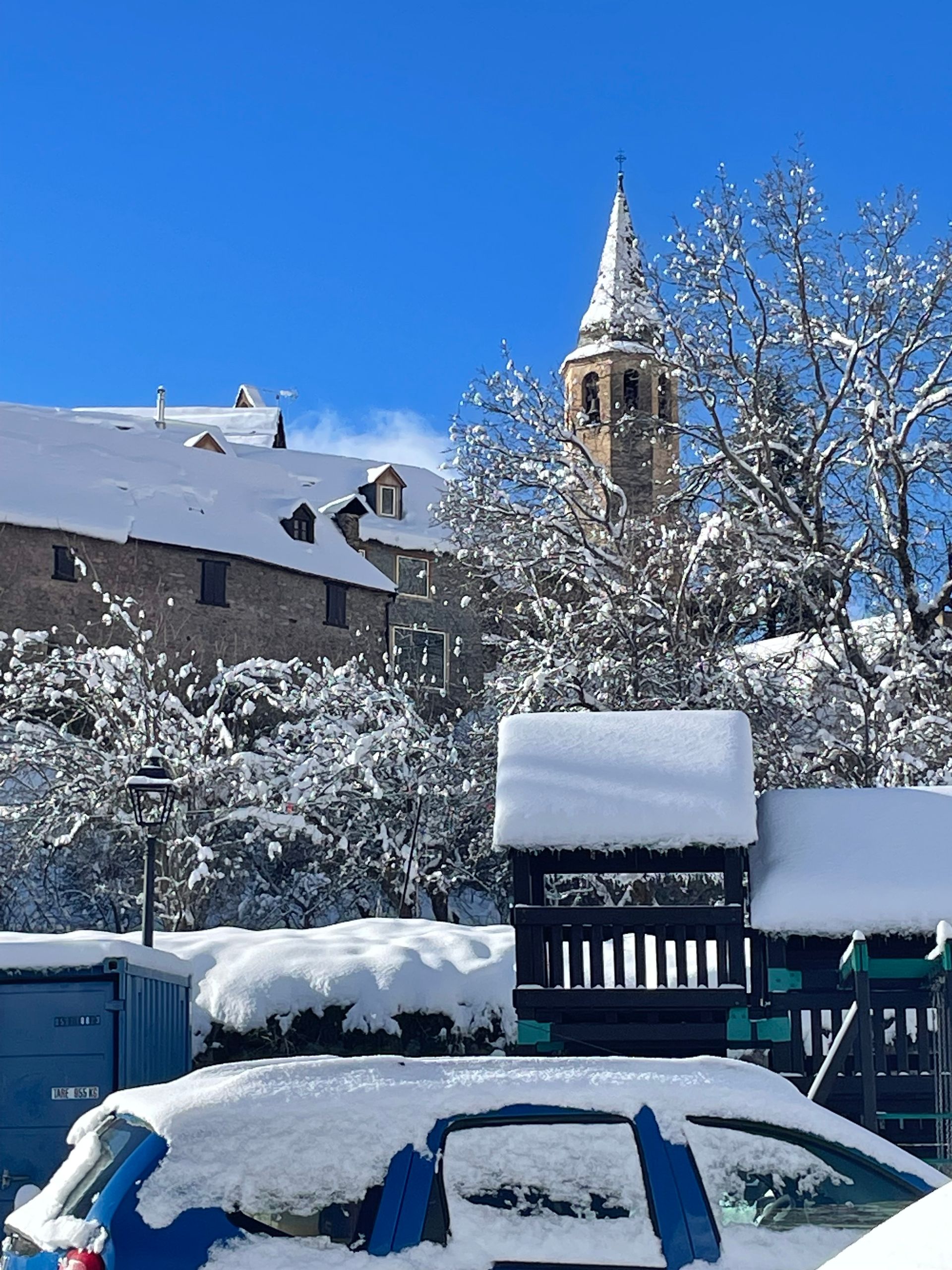 Un coche está cubierto de nieve con una iglesia al fondo.