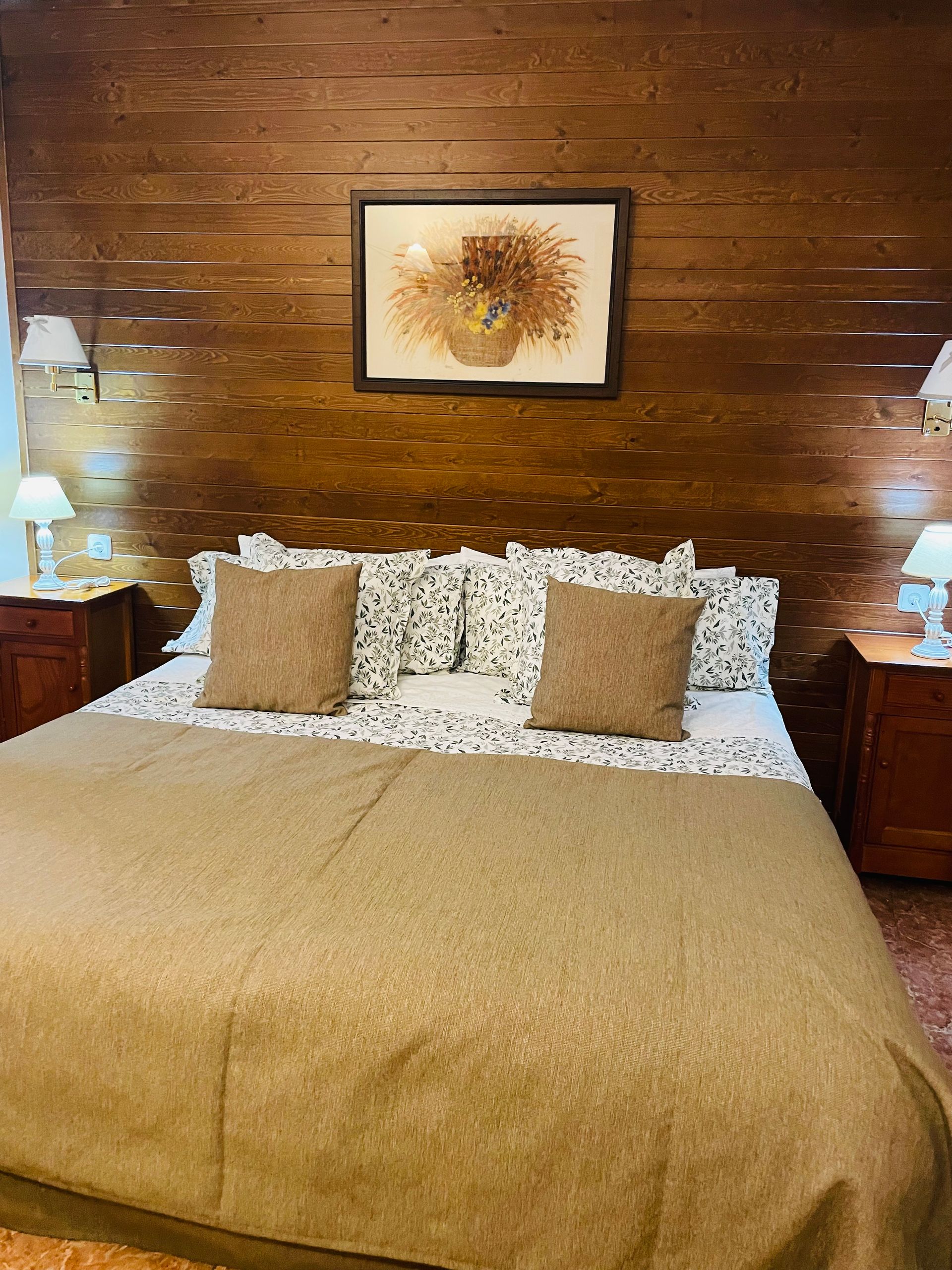 Un dormitorio con una cama, mesitas de noche, lámparas y un cuadro en la pared encima de la cama.