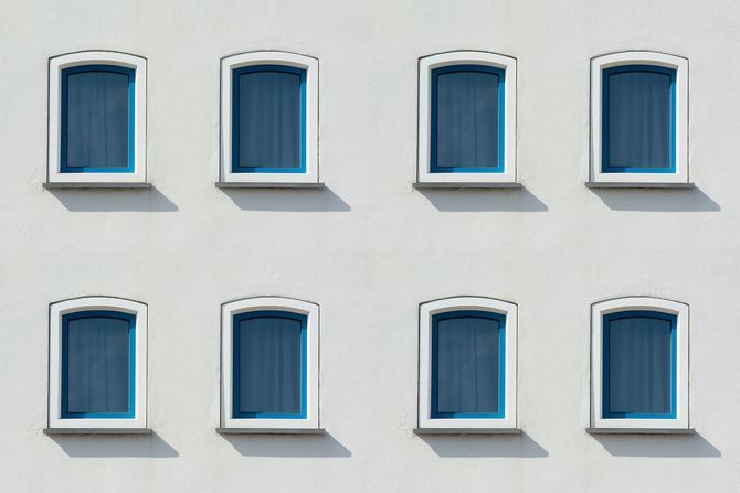 Eight blue windows on a white building facade, arranged in two rows.
