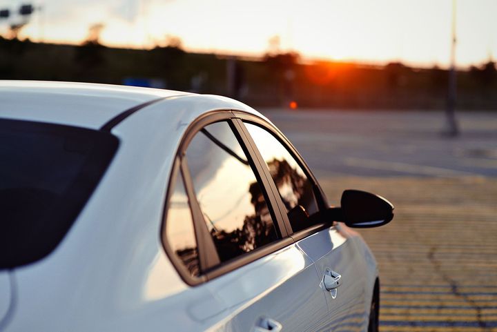 White car parked at sunset, with rear window and side mirror reflecting the orange sky.