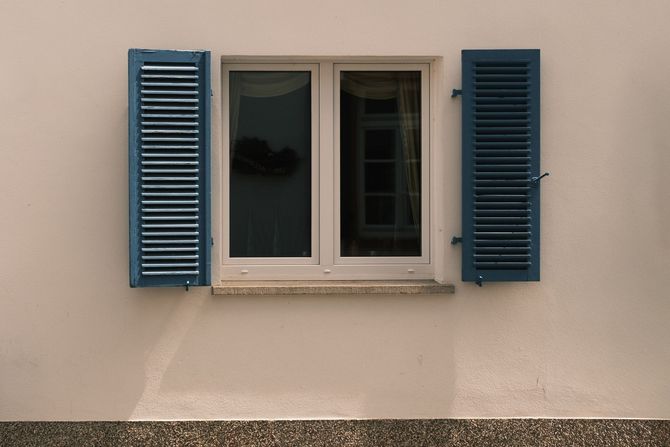 Beige wall with a centered window and blue shutters on both sides