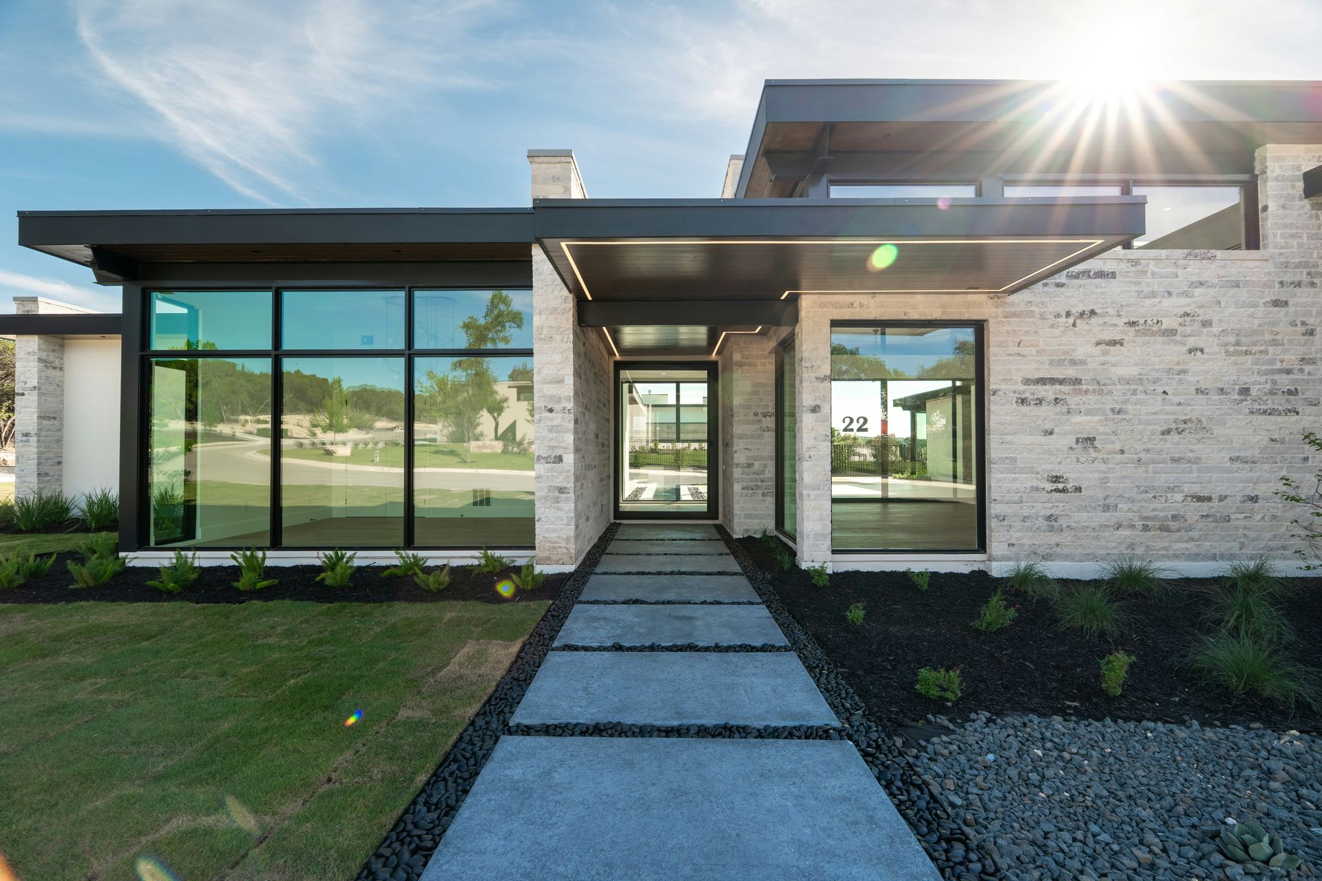 Modern single-story house with stone facade, large windows, and a front walkway in bright sunlight
