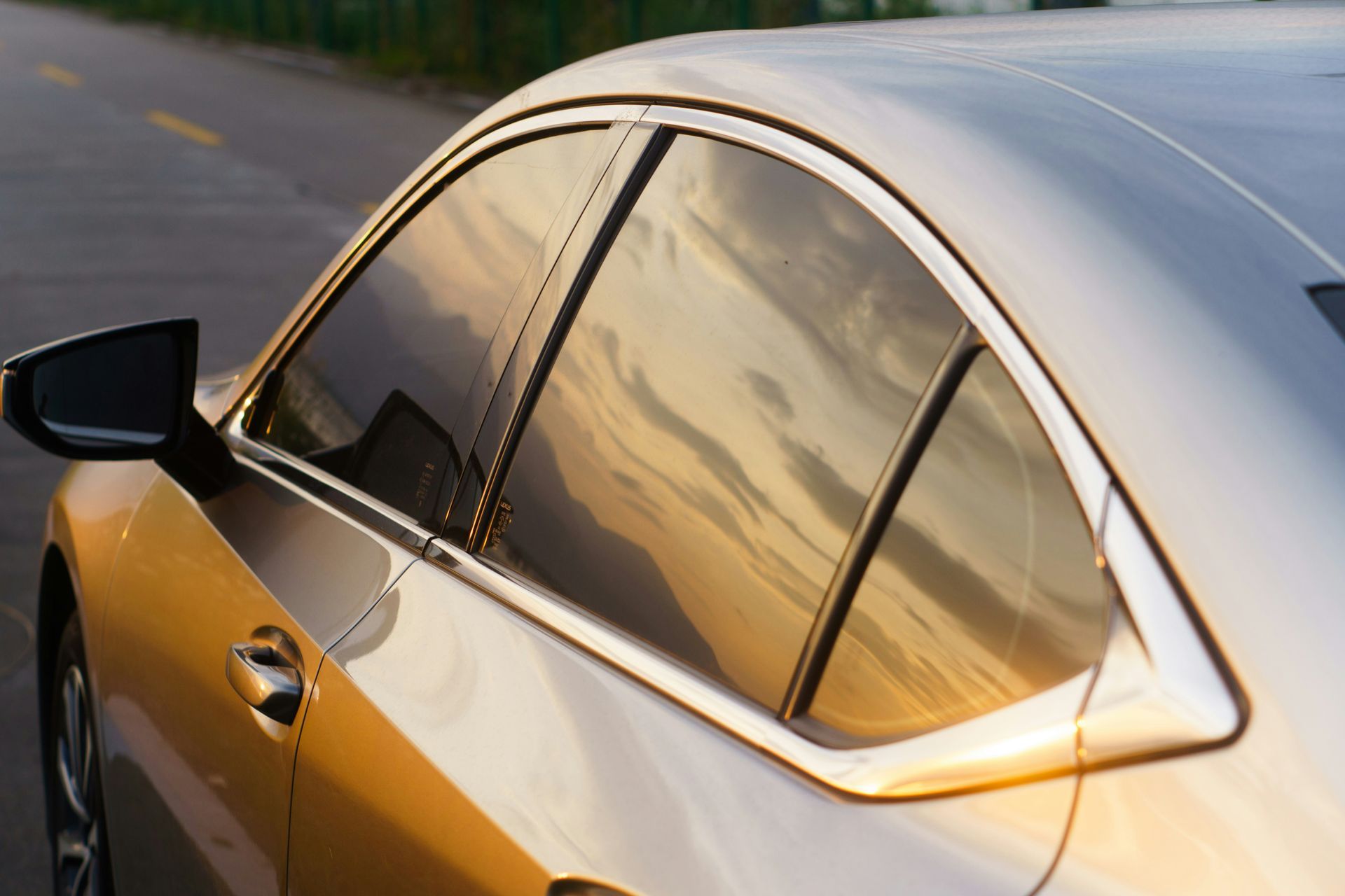 Side view of a silver car with tinted windows reflecting a sunset on a road