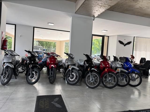 Motocicletas alineadas en una luminosa sala de exposición con columnas blancas y suelo de baldosas.