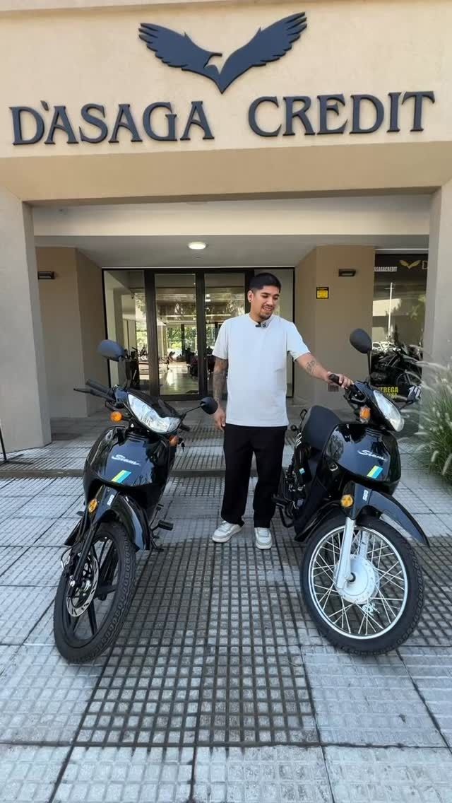 Un hombre de pie entre dos motocicletas frente a una tienda de D'SAGA CREDIT.