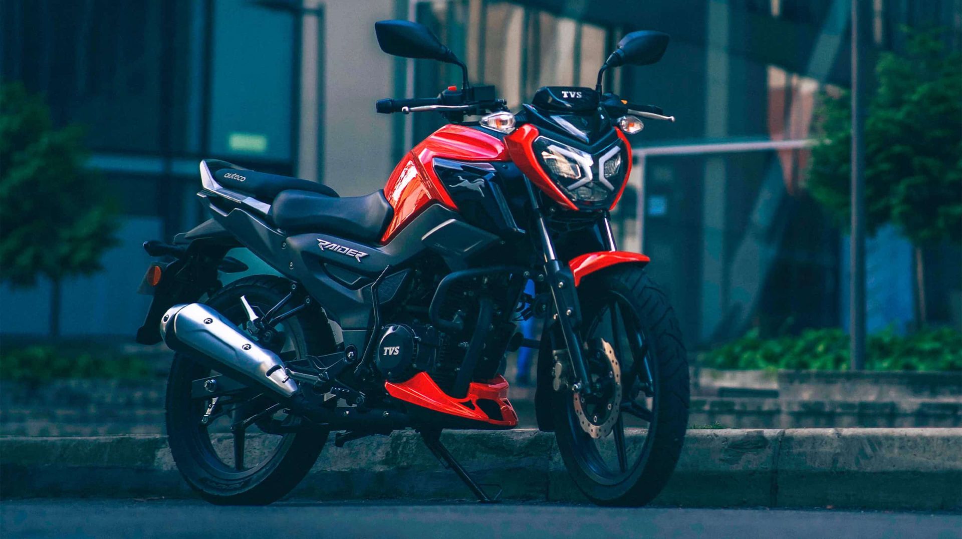 Una motocicleta roja y negra estacionada en una calle mojada frente a un edificio moderno.