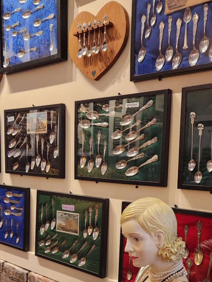 Display of silver spoons in framed shadow boxes on a wall, with a blonde mannequin in the foreground.