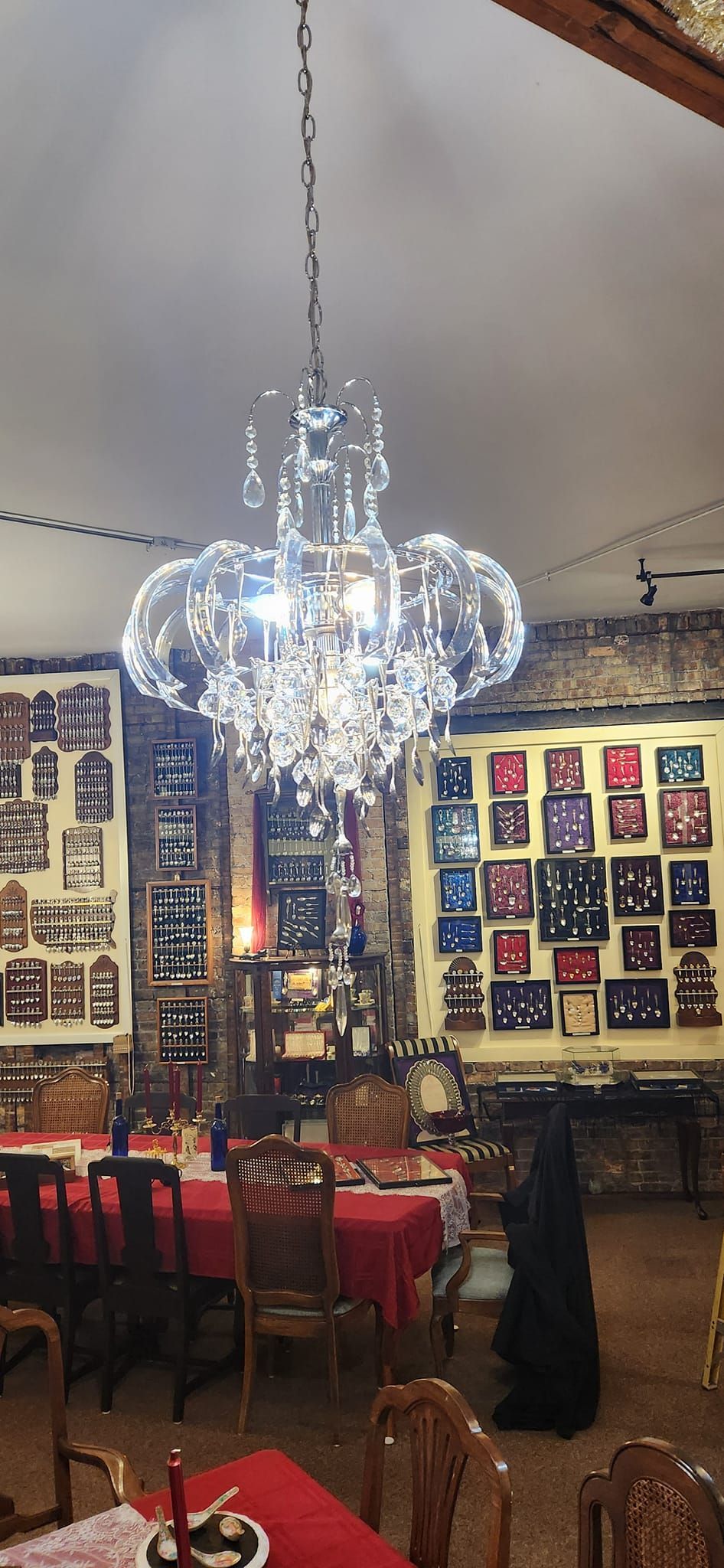 Crystal chandelier hangs over a dining area with red tablecloths, framed art on the walls.