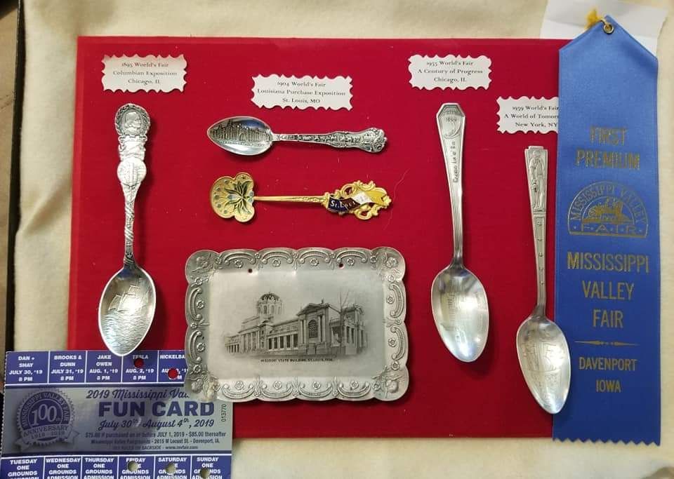 Display of antique spoons and a tray on a red background, with a fair ribbon and fun card.