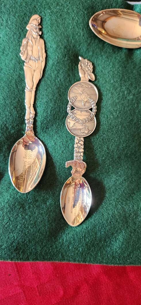 Two ornate silver spoons on green and red fabric, with a small plate in the upper right.