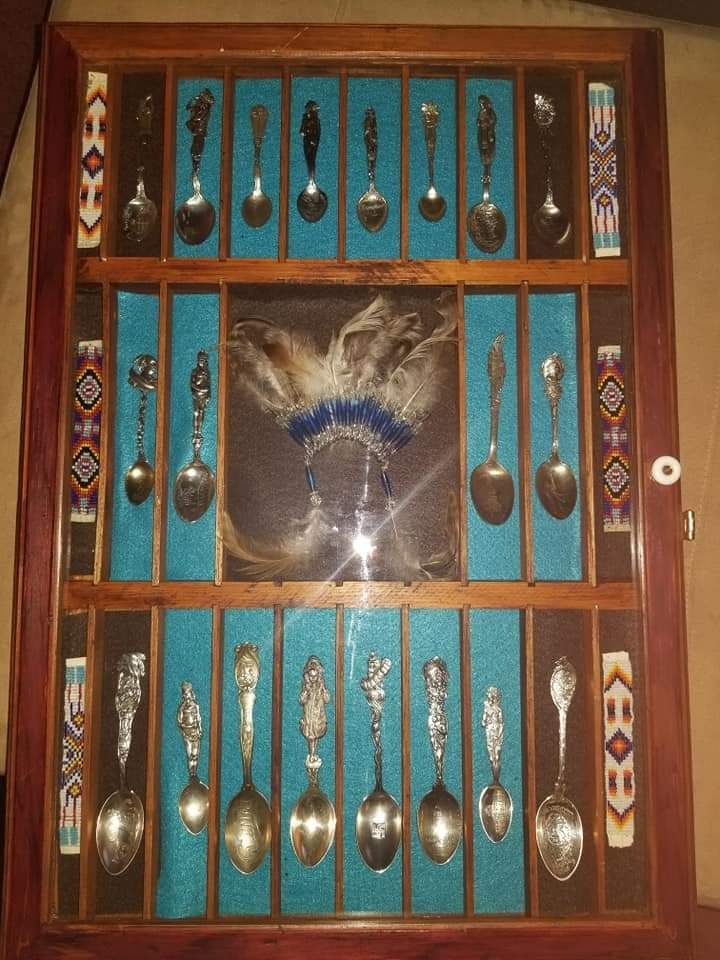 Display case with silver spoons and Native American artwork on a blue background.