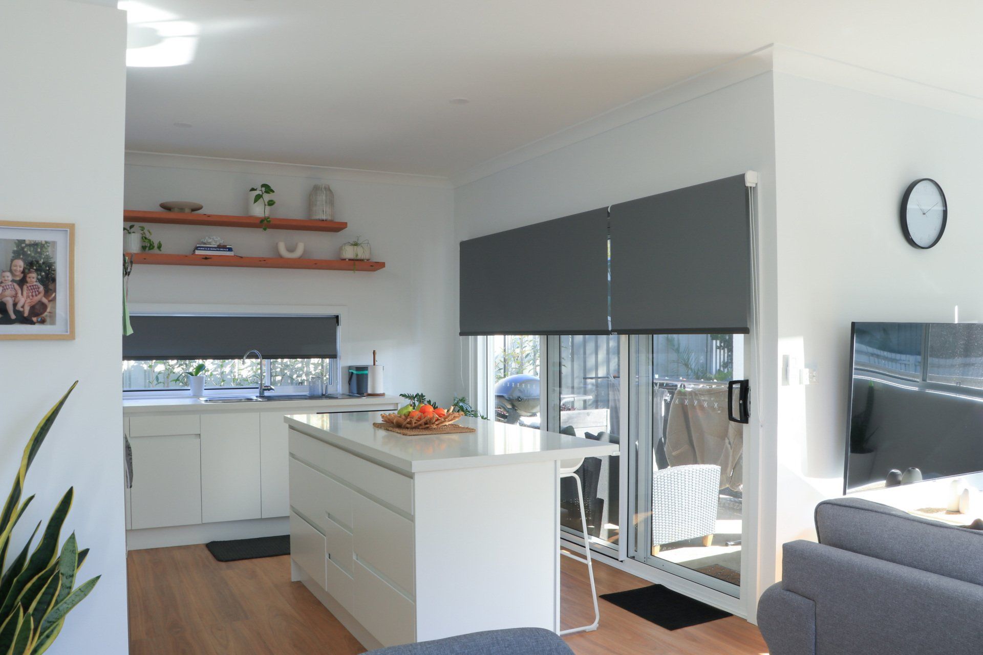 A living room with a kitchen and a clock on the wall.