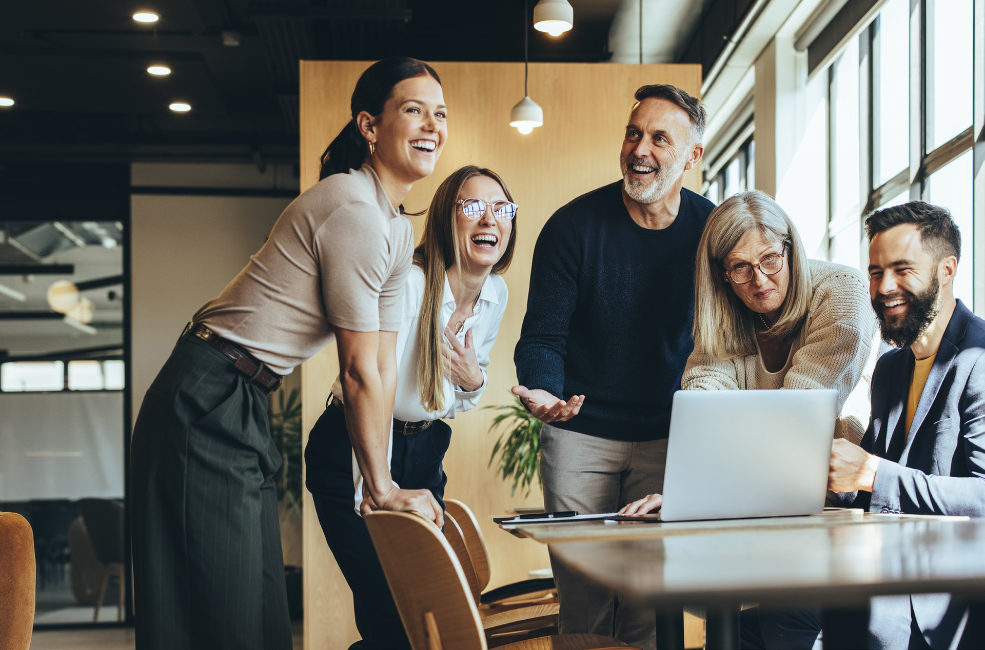 A group of people are standing around a table looking at a laptop computer.