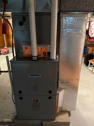 Gray furnace with two silver ducts in a basement beside a wrapped insulated air duct.